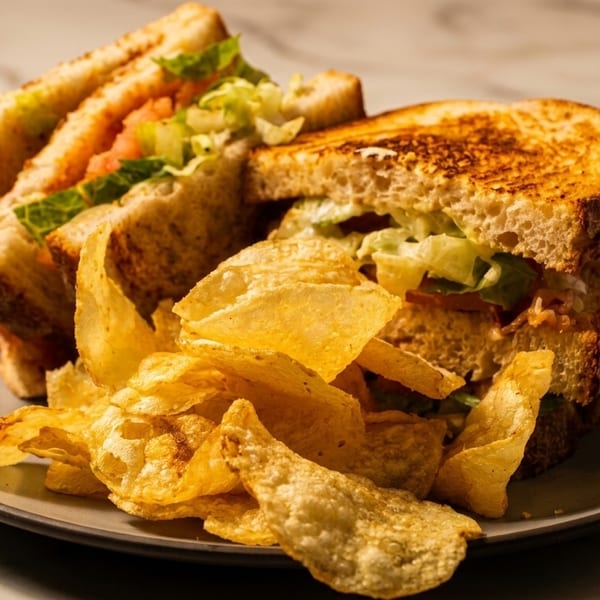 Toasted sandwich with lettuce and tomato, served with a side of golden potato chips on a plate.